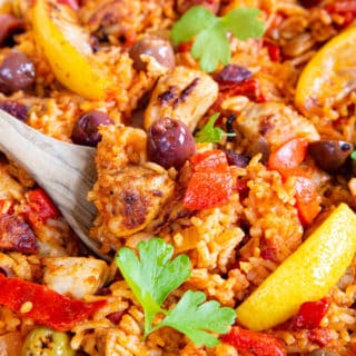 A close up of Spanish chicken and rice, with olives, peppers and lemon wedges