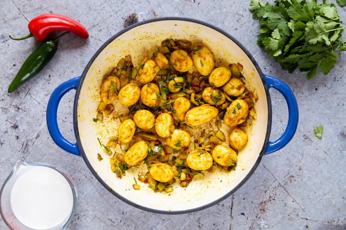 A top down view of a skillet containing fried onion, garlic, chilli, spices, coriander leaves and potatoes