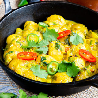 A cast iron dish of golden yellow potato curry garnished with coriander and fresh chillis