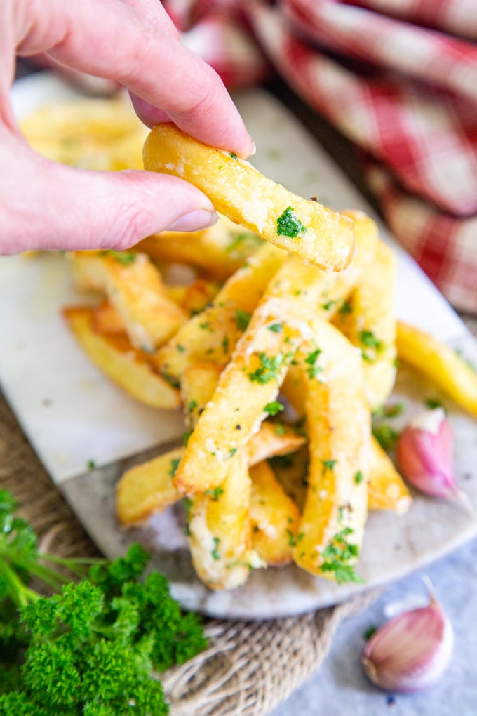 A hand takes a single chip from a serving of garlic Parmesan fries.