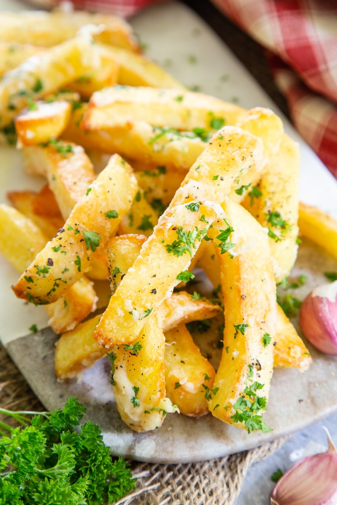 A close up of golden garlic Parmesan fries with a garnish of chipped parsley.
