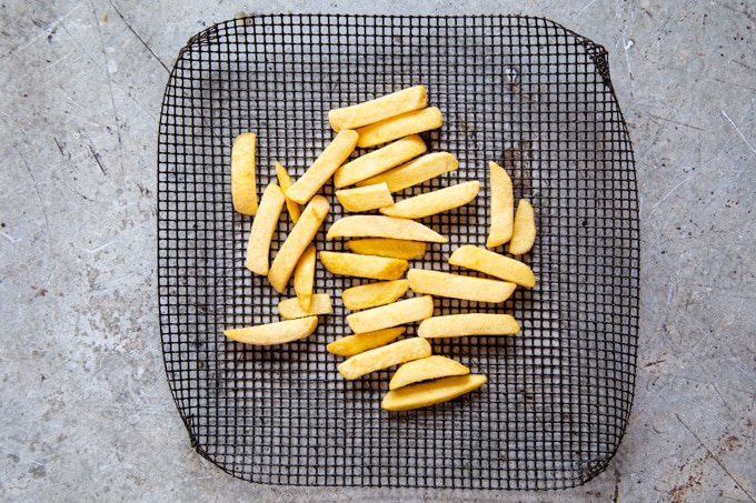 A mesh baking tray of frozen oven chips, ready to bake.