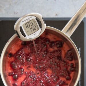 A thermometer showing a saucepan of red jam boiling at 105°C