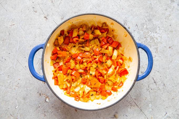 Spiced added to gently cooked pepper, onions and garlic in a shallow blue casserole dish.