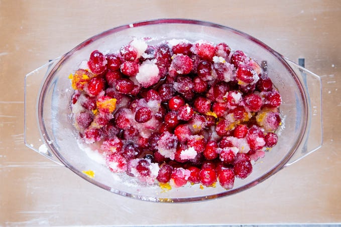 A glass ovenproof dish of mixed cranberries, sugar and orange zest, ready to bake.