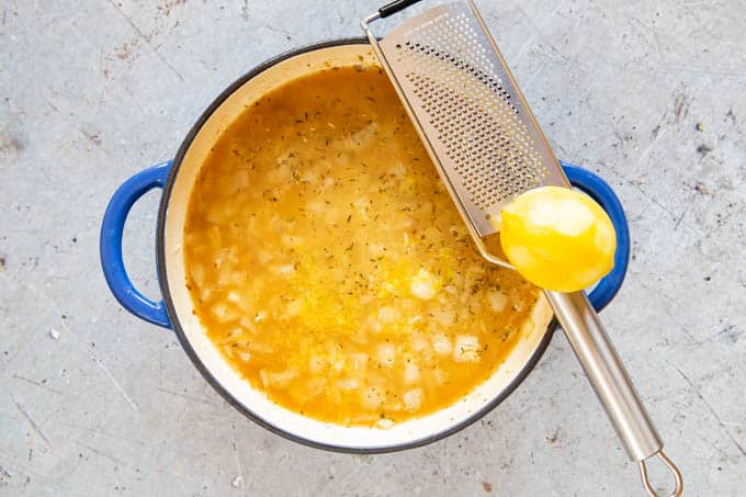 A top down photo of a pan of rice and stock, with a lemon zester and fresh lemon balanced on the side. 