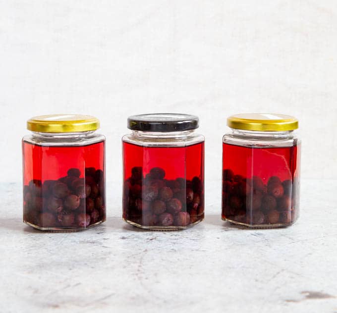 Three jam jars of sloes and gin; the liquid is all the same pale red colour.