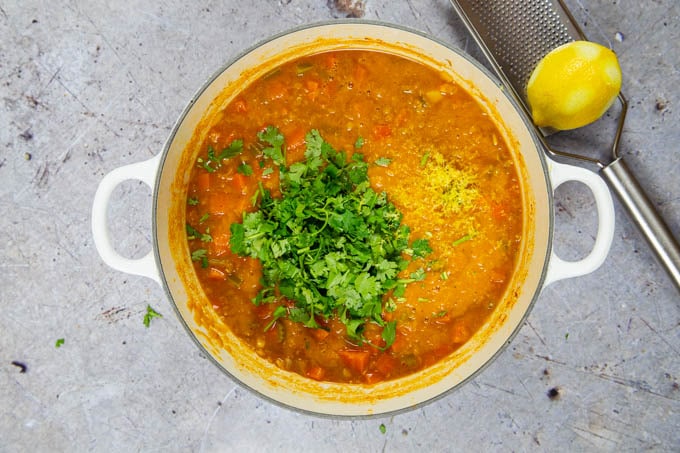 Top down picture of a casserole of carrot and lentil soup, with handful of chopped coriander added.