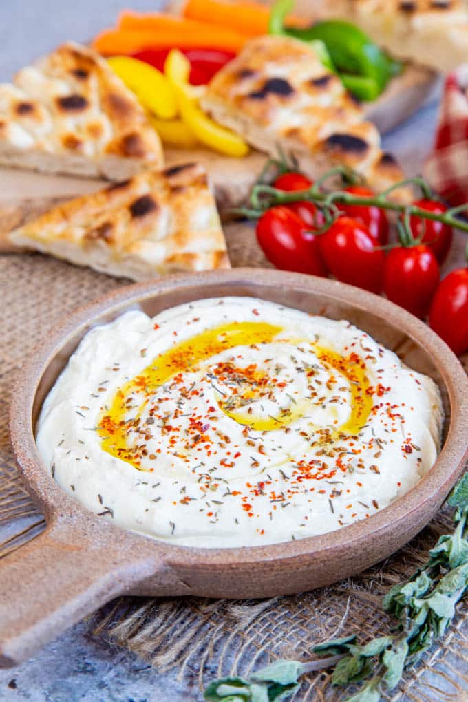 A ceramic bowl of whipped feta dip, garnished with spices and olive oil. Bread and crudities in the background