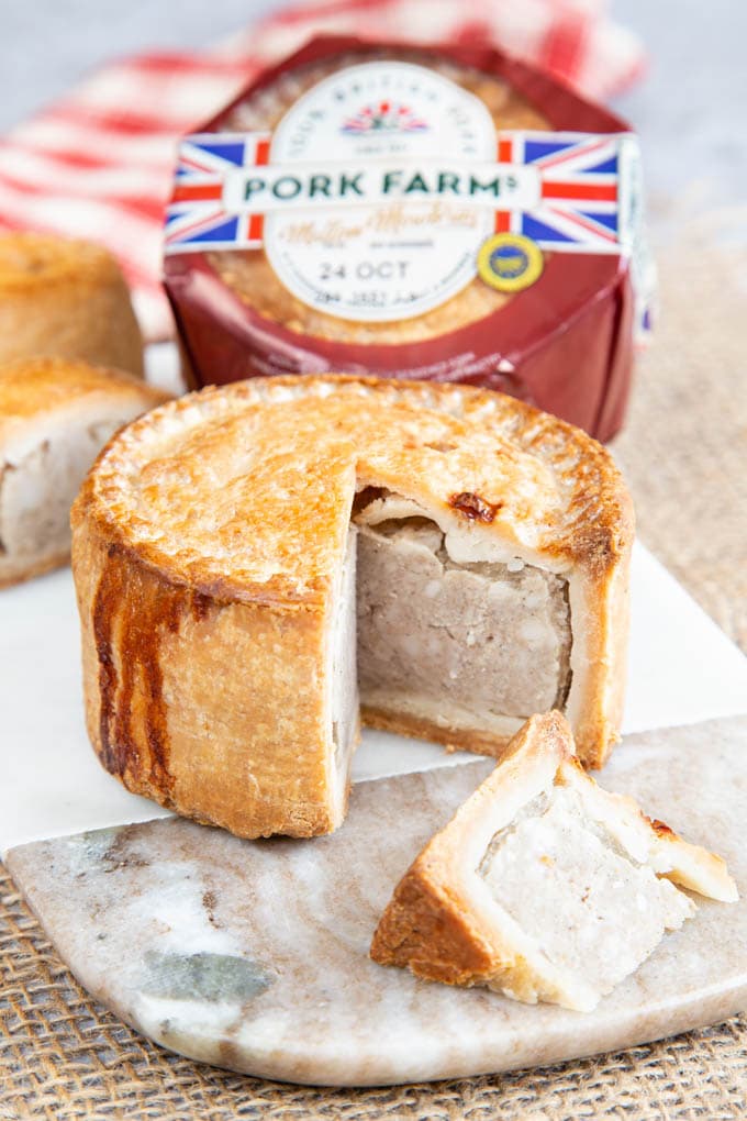 A close up of a pork pie cut open on a marble board. Another pie, in its packet, in the background.