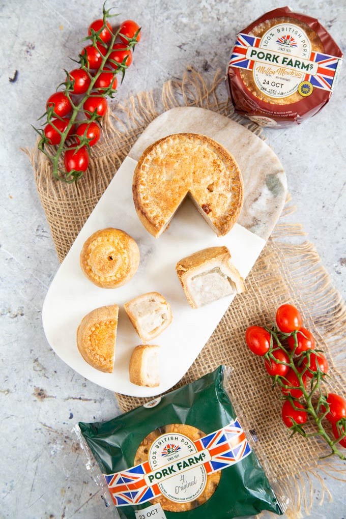 A top down picture of pork pies, large and small, whole and cut, on a marble board.