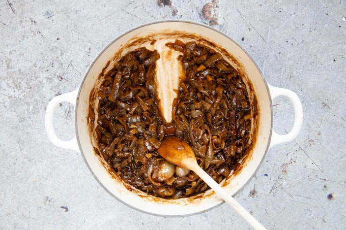Dark brown cooked onion marmalade. A wooden spoon leaves a trace across the bottom of the pan.