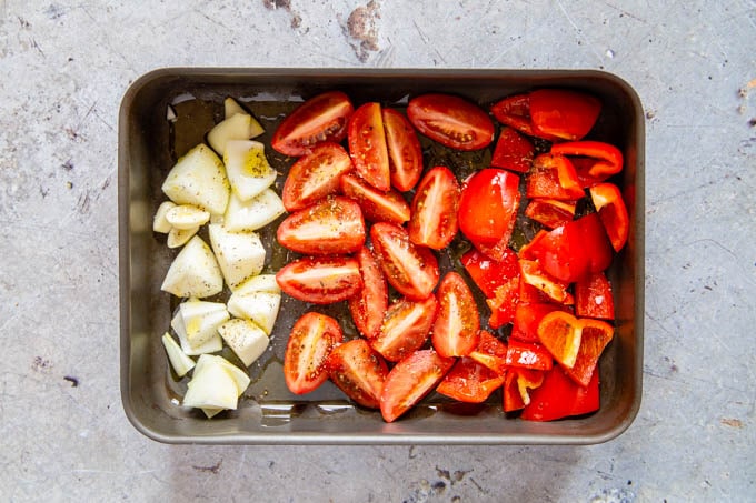Vegetables in a roasting tray - onion, tomato and red peppers, ready to roast.