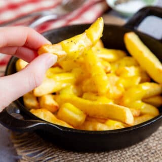 Close up of cheesy chips being taken from a serving dish full.