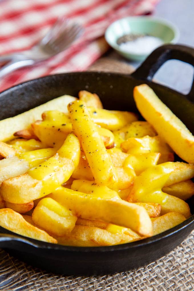 A black dish full of yellow cheesy chips covered in rich sauce.
