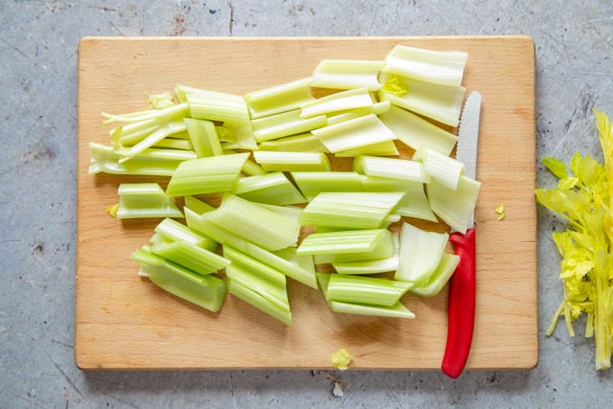 Celery stalks cut into pieces on a wooden chopping board.