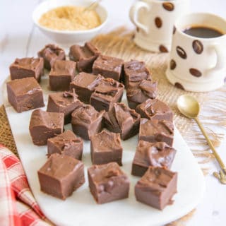Cubes of coffee fudge on a marble chopping board. Espresso cups of coffee and a small bowl of sugar in the background.