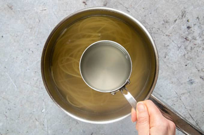 Taking a cup full of pasta water from cooking pasta, using a miniature saucepan.