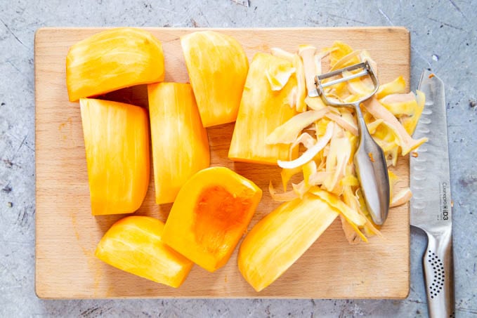 A board with a butternut squash, cut into eight, being peeled.