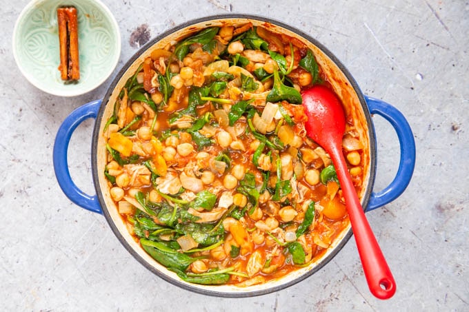 Top down picture of turkey tagine with wilted spinach, ready to serve. A stick of cinnamon has been removed from the dish and placed next to it in a small bowl.