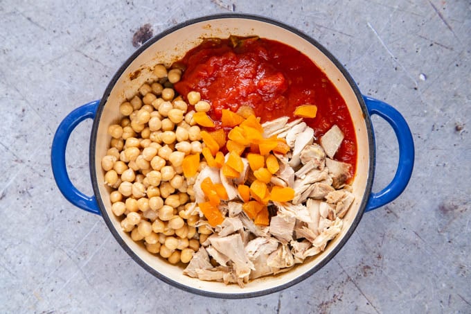 The ingredients - chickpeas, tomatoes, honey, chicken, stock and apricots are added to the pan.