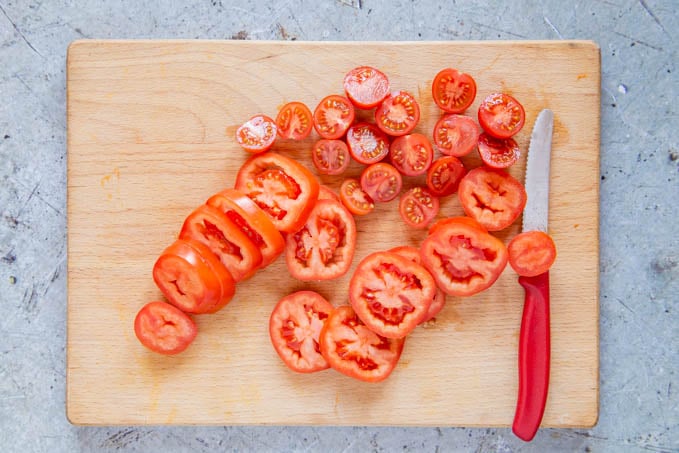 Sliced cherry and plum tomatoes on a wooden board. A serrated knife lies next to the tomatoes.