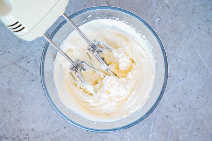 A top down picture of a hand mixer in a glass bowl, full of cream whipped to the soft peak stage.