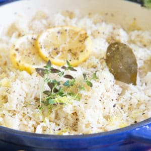 Close up picture of Greek rice with lemon slices, pepper, a sprig of thyme and a bay leaf.