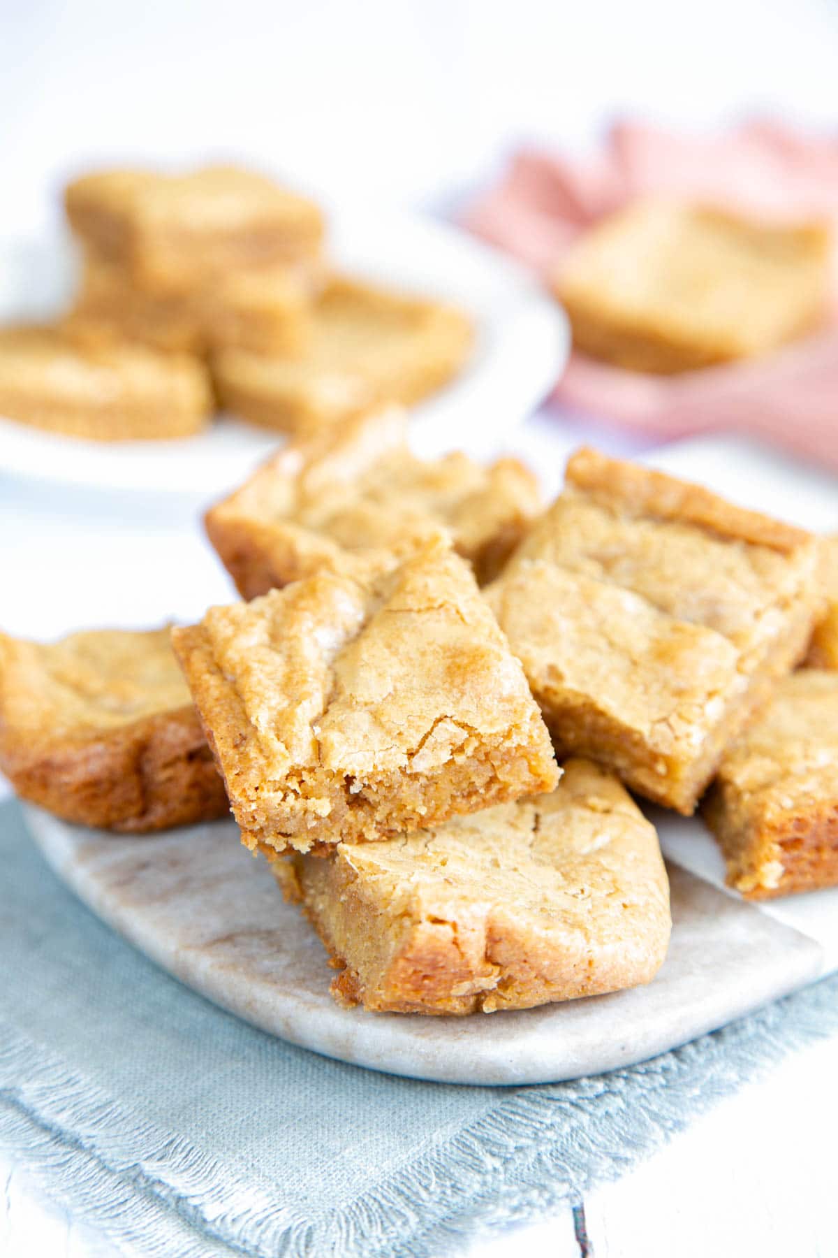 A close up of some blondies arranged on a marble board. More blondies in the background.