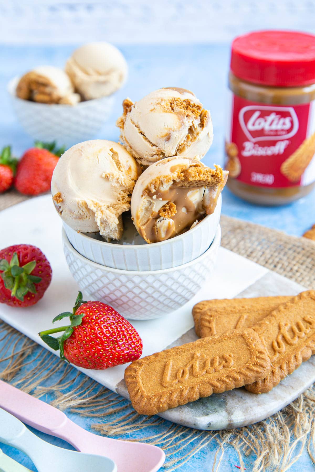 Three scoops of speculoos ice cream in a small white bowl. A jar of Lotus biscoff speculoos spread in the background.