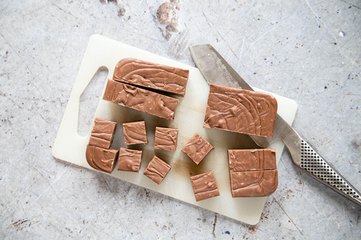 Cutting fudge into bite-sized pieces. The block of fudge on a white chopping board is half cut into 2cm squares.