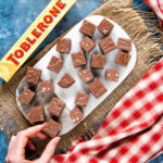 Top down picture of a marble board evenly covered with pieces of fudge. In the bottom left corner, a hand is taking a piece of fudge.