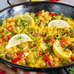 Close up of golden yellow paella showing lemon wedges, olives, and sliced peppers.