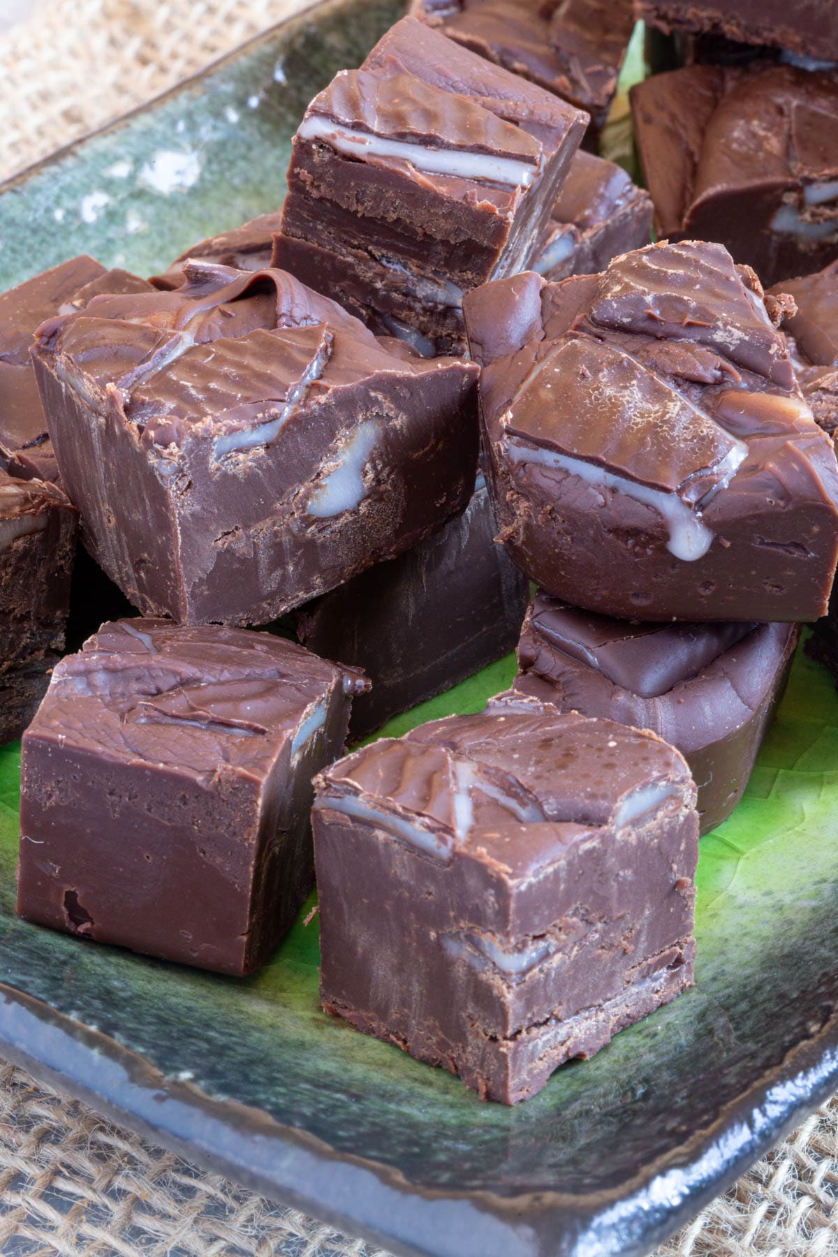 Close up of pieces of fudge stacked two high on a green and black plate. Broken up pieces of After Eight are oozing mint filling.