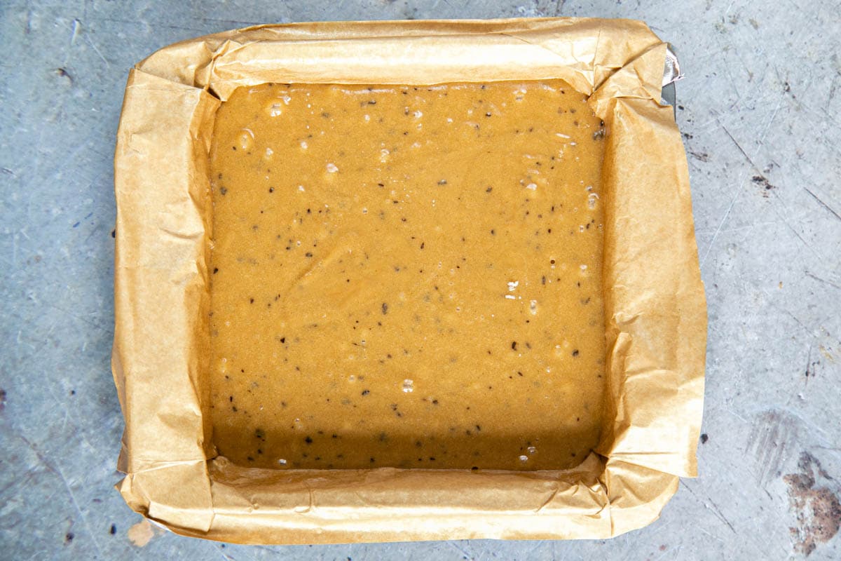 The blondie batter has bee poured into a lined square roasting tray