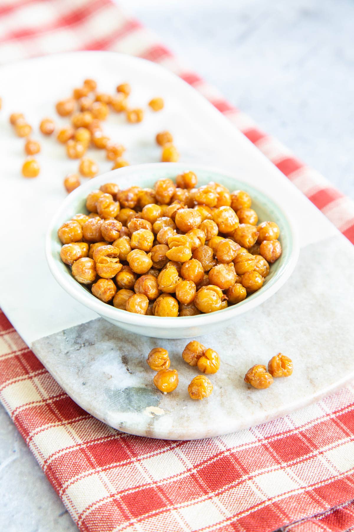 A small bowl of roasted chickpeas presented on a marble board. More chickpeas dot the board.