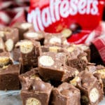 A close up of pieces of fudge with a red chocolate packet out of focus in the background.