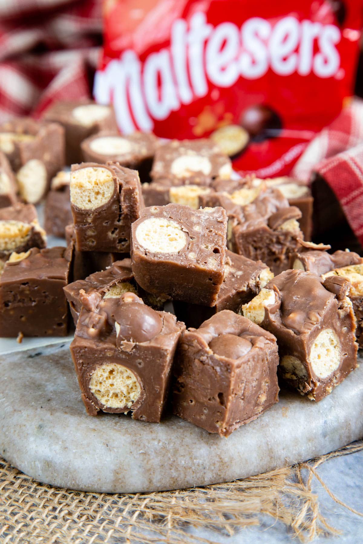 Cubes of Malteser fudge on a marble board, showing the whole maltesers stirred through the fudge. A red Malteser bag is in the background.