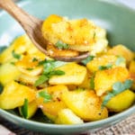A wooden spoon with a few slices of golden crispy potato held above a green bowl with more potatoes