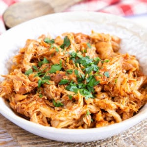 Close up of shredded chicken, garnished with chopped parsley.