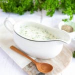 Close up of parsley sauce in a white jug, served on a marble board and a small wooden spoon.