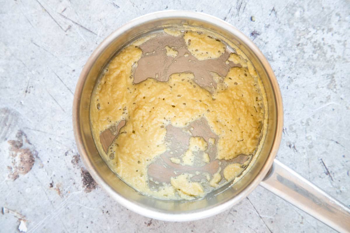 Making a roux: flour and melted butter stirred together and cooked. There are signs of small bubbles in the mixture, which doesn't cover the bottom of the pan.
