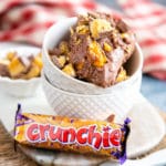 A close up of a serving of delicious chocolatey Crunchie ice cream, in the top of two stacked bowls. In front of the bowls is an unopened Crunchie bar.