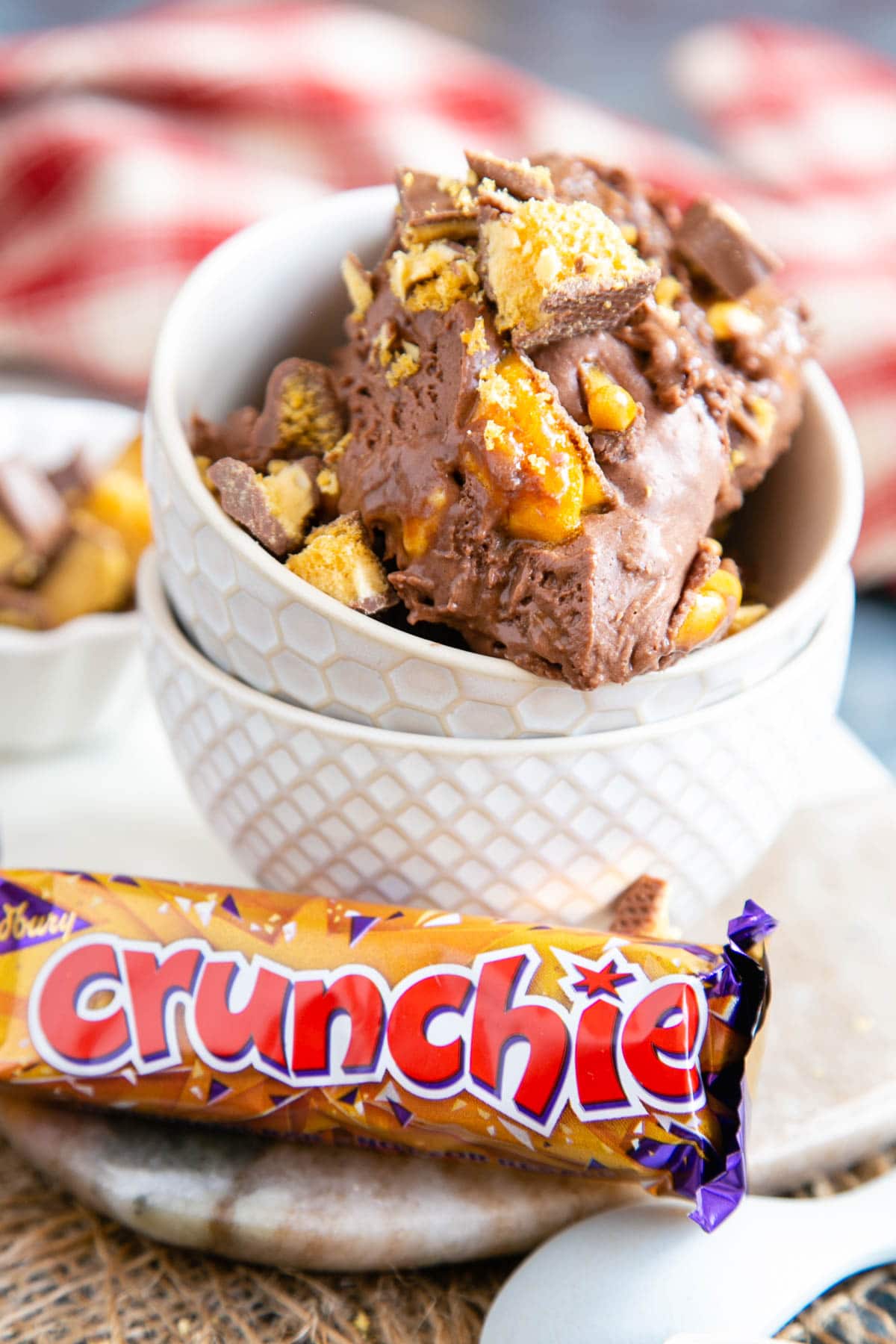 Two stacked bowls, the top containing delicious Crunchie ice cream. In front of the bowls is an unopened Crunchie bar.