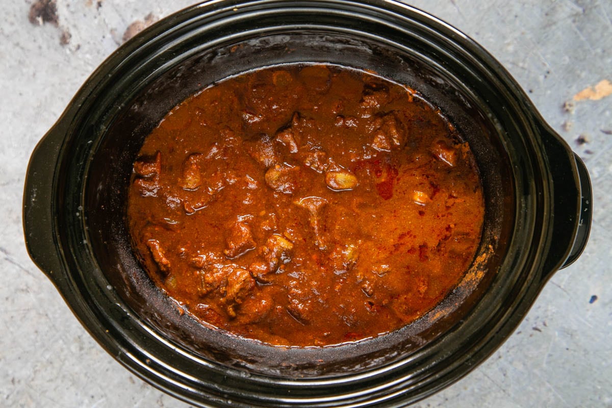 Cooked beef curry in a slow cooker. The curry is dark red, shiny and looks delicious.