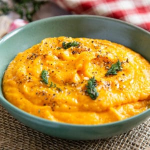 Butternut squash mash, glossy and tempting in a green bowl, garnished with salt, pepper and thyme.