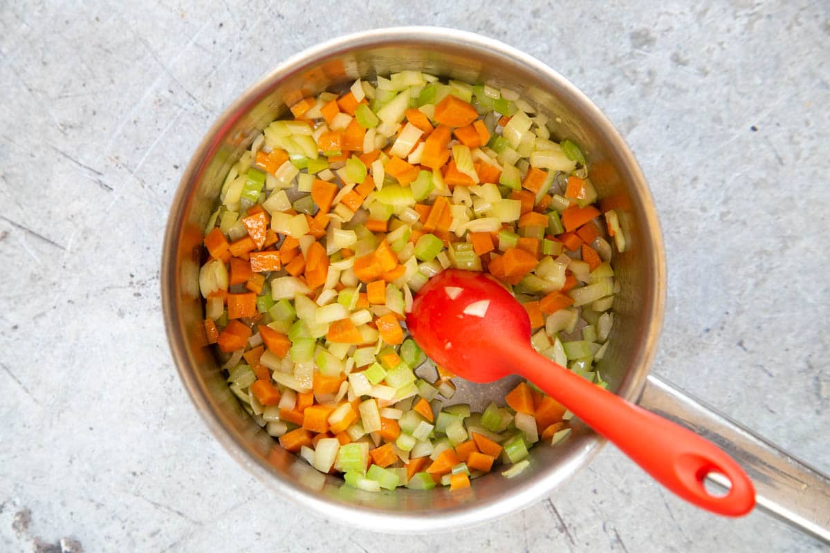 Celery, carrot and onion in a saucepan, ready to make a soffrito base for soup. Coated in the olive oil, they are starting to cook.