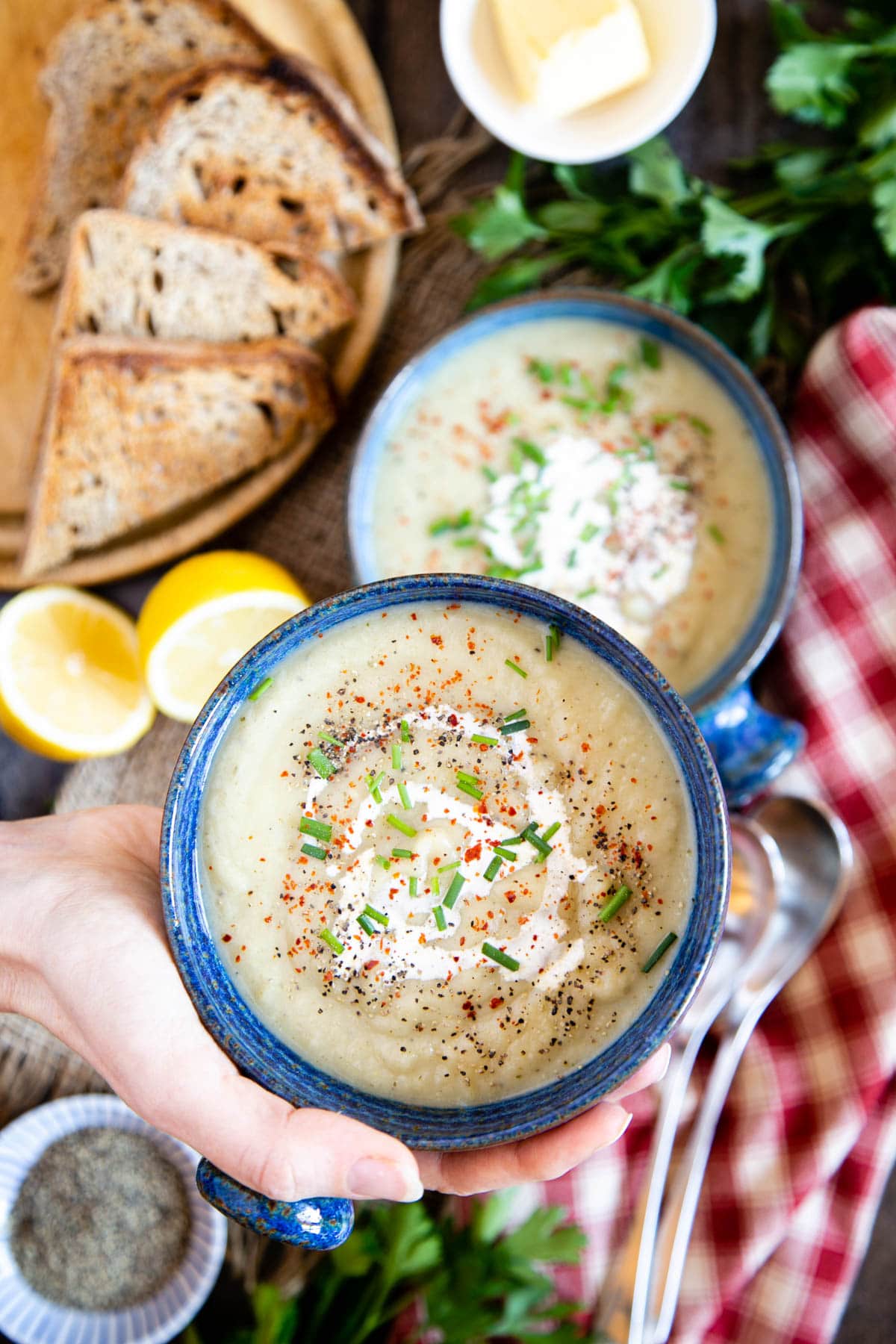 A warming bowl of celeriac soup held up to the viewer; it is prettily garnished and served with toast.