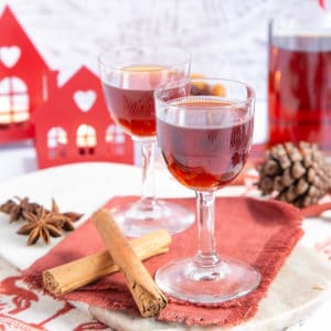 Close up of of tawny-red Christmas gin in pretty glasses, the tray decorated with cinnamon and star anise.