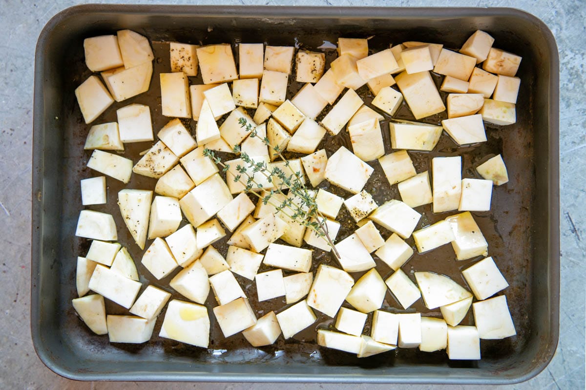 The celeriac cubes have been trasferred to a roasting tin with the oil, thyme and seasoning.